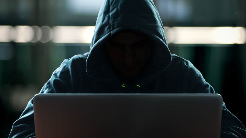 Vermummte Person mit Kaputzenpullover sitzt an einem Laptop